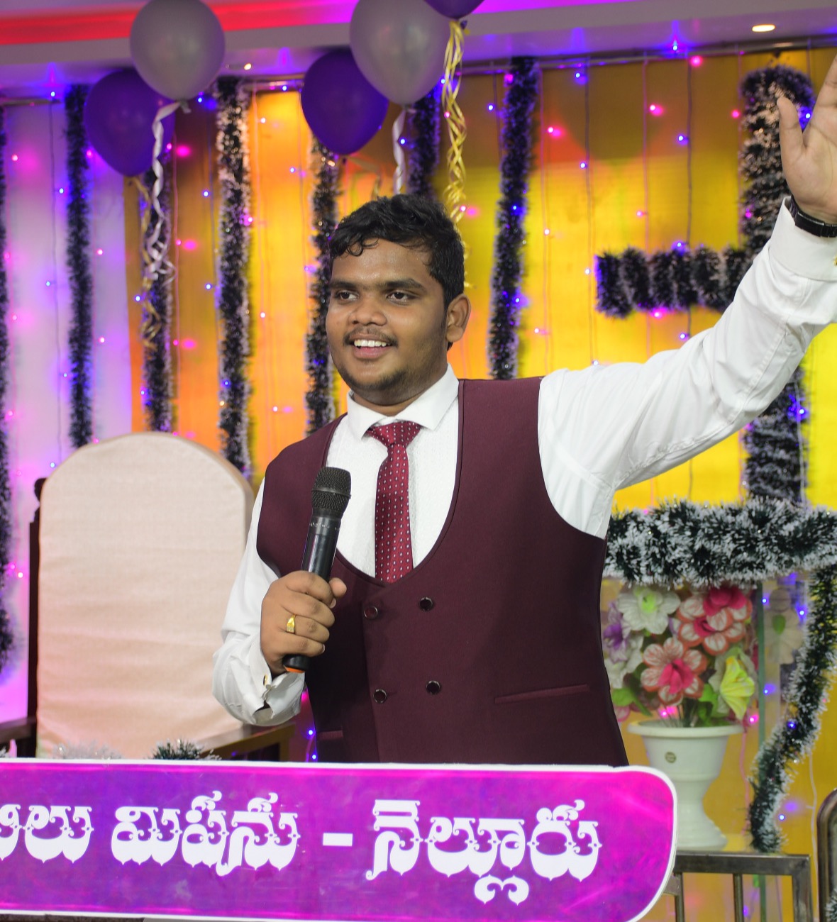 Akshai Kumar Pammi preaching on stage with a microphone, hand raised